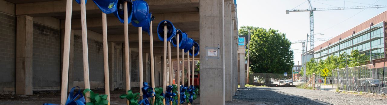 Construction hats sit on top of shovels with crane in background.