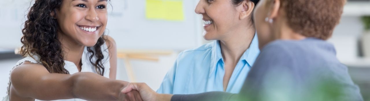 A woman smiles while shaking hands with an HR representative.