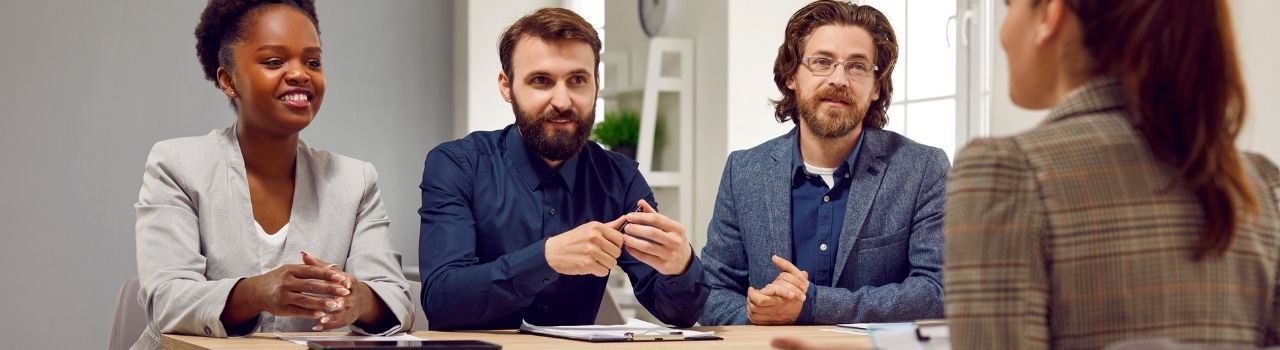 Three employees smile while meeting with HR representative in meeting.
