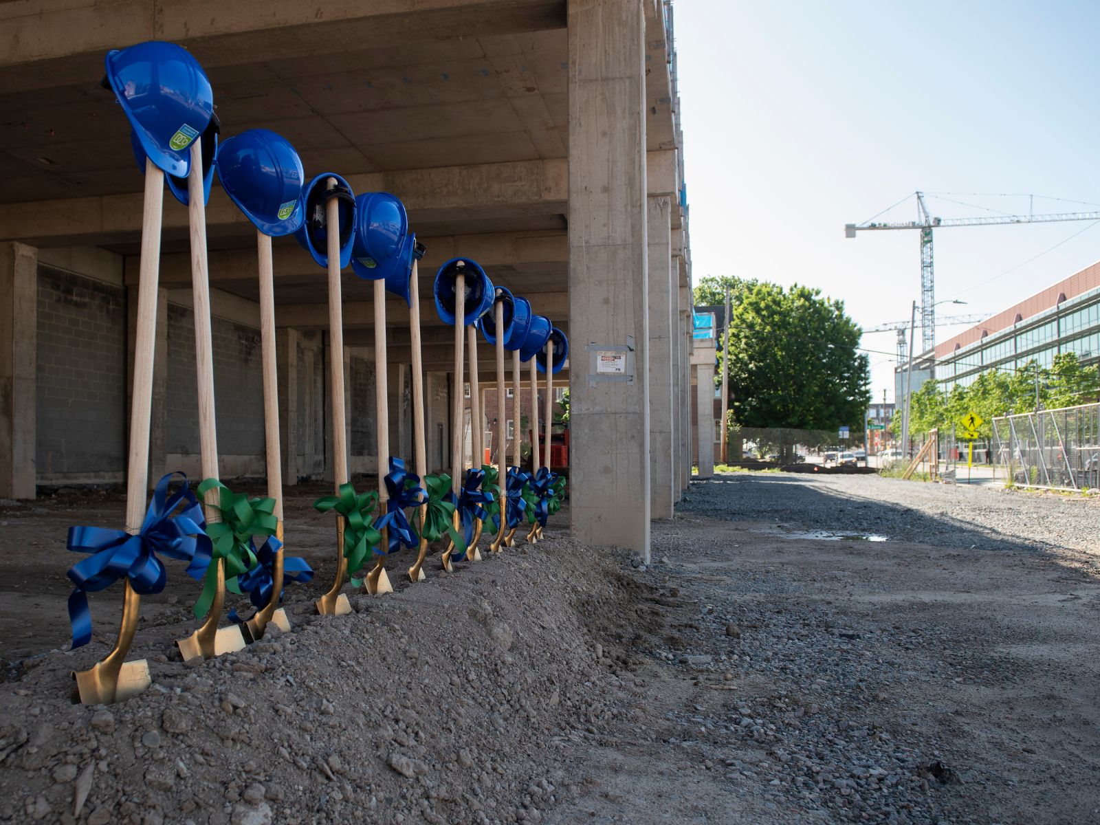 DCo Transition Groundbreaking Helmets on shovels. Buildings in background under construction